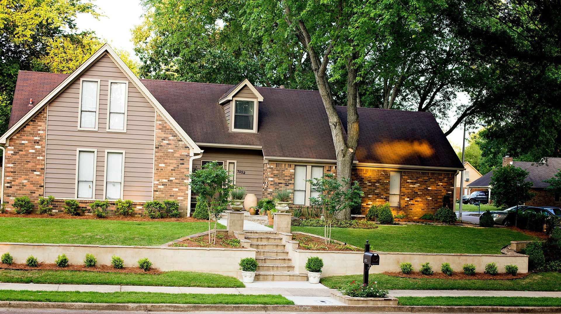 a large brick house with a brown roof is sitting on a lush green lawn .