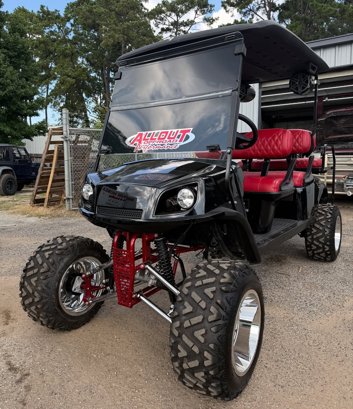 Black, customized golf cart with large tires and red interior, parked outside.