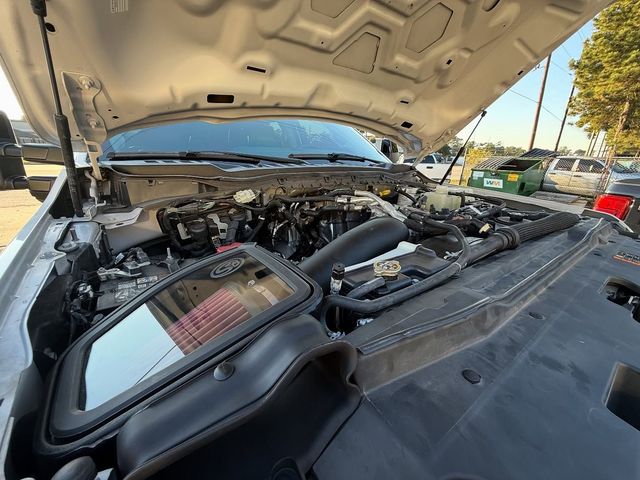 Car engine with the hood open, revealing components like the air filter and engine block in an outdoor setting.