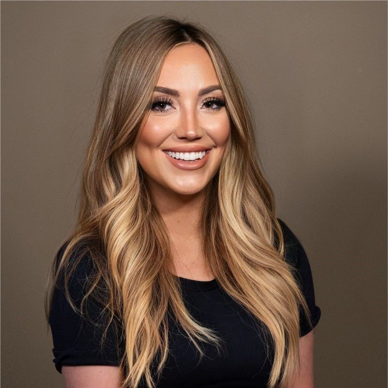 A woman with long blonde hair is wearing a black shirt and smiling.