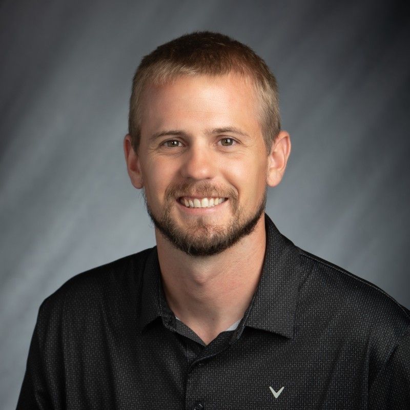A man with a beard is wearing a black shirt and smiling for the camera.