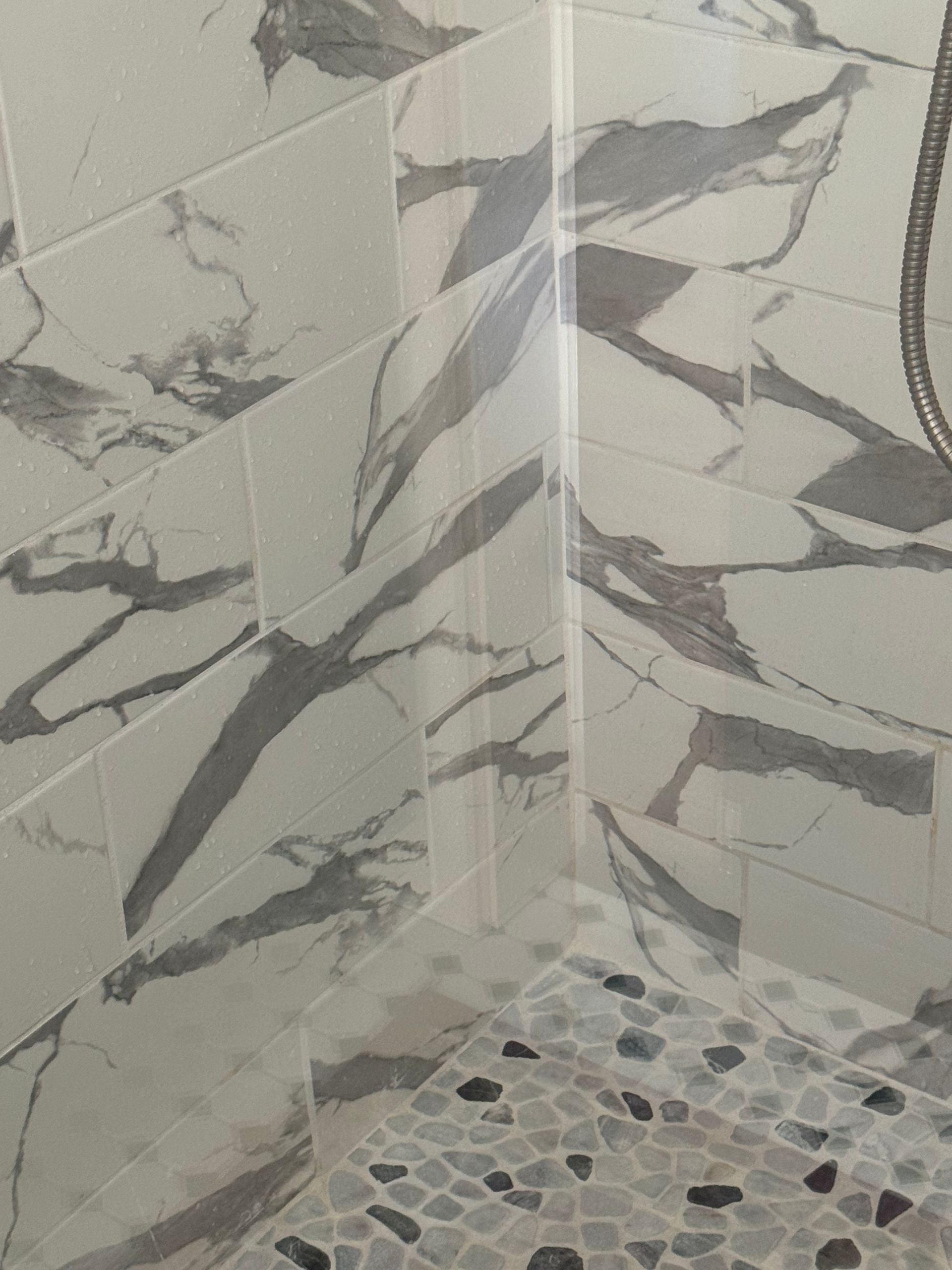 A shower with marble tiles and a pebble floor.
