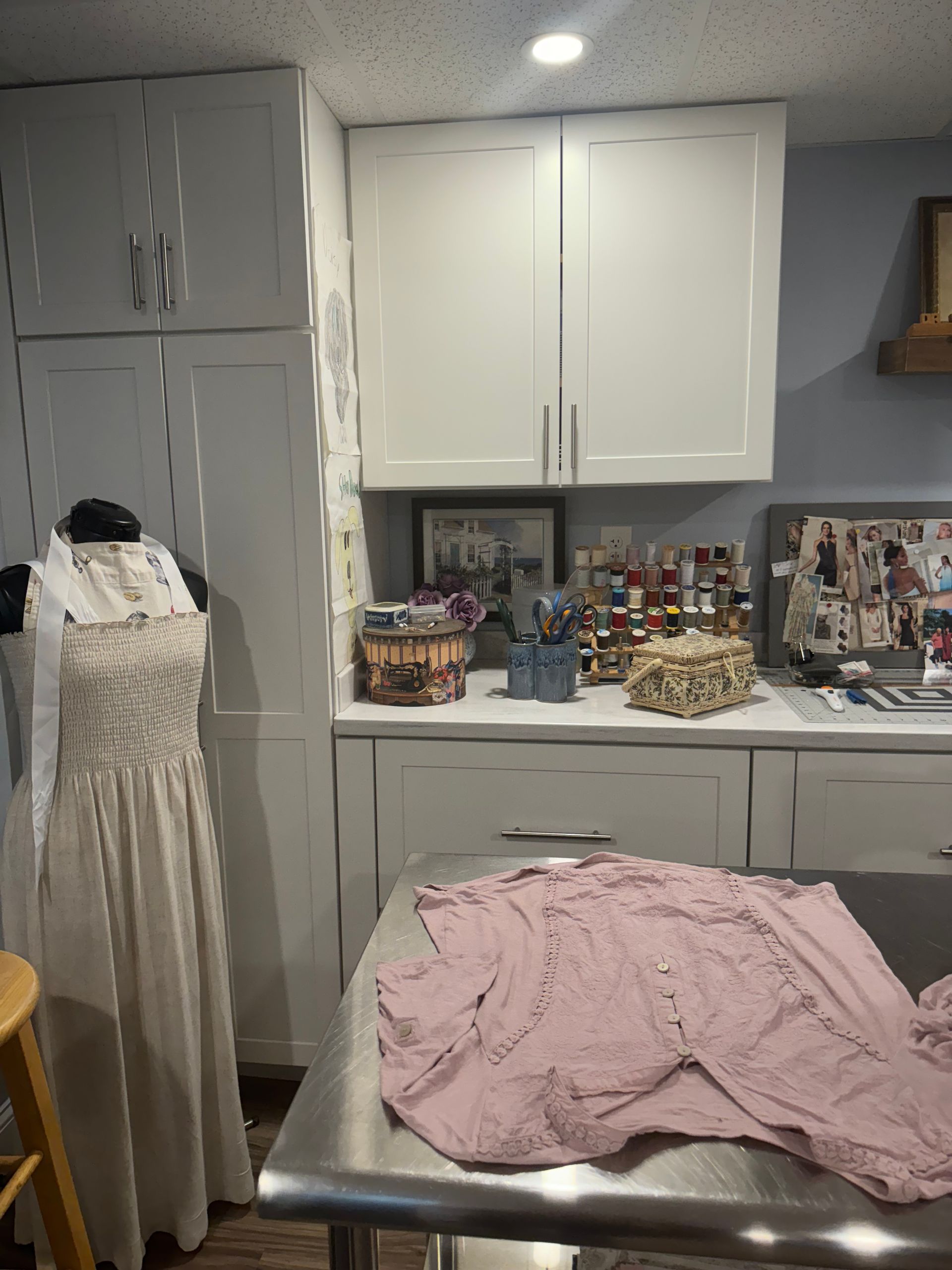 A pink shirt is sitting on a table in a sewing room with white cabinets