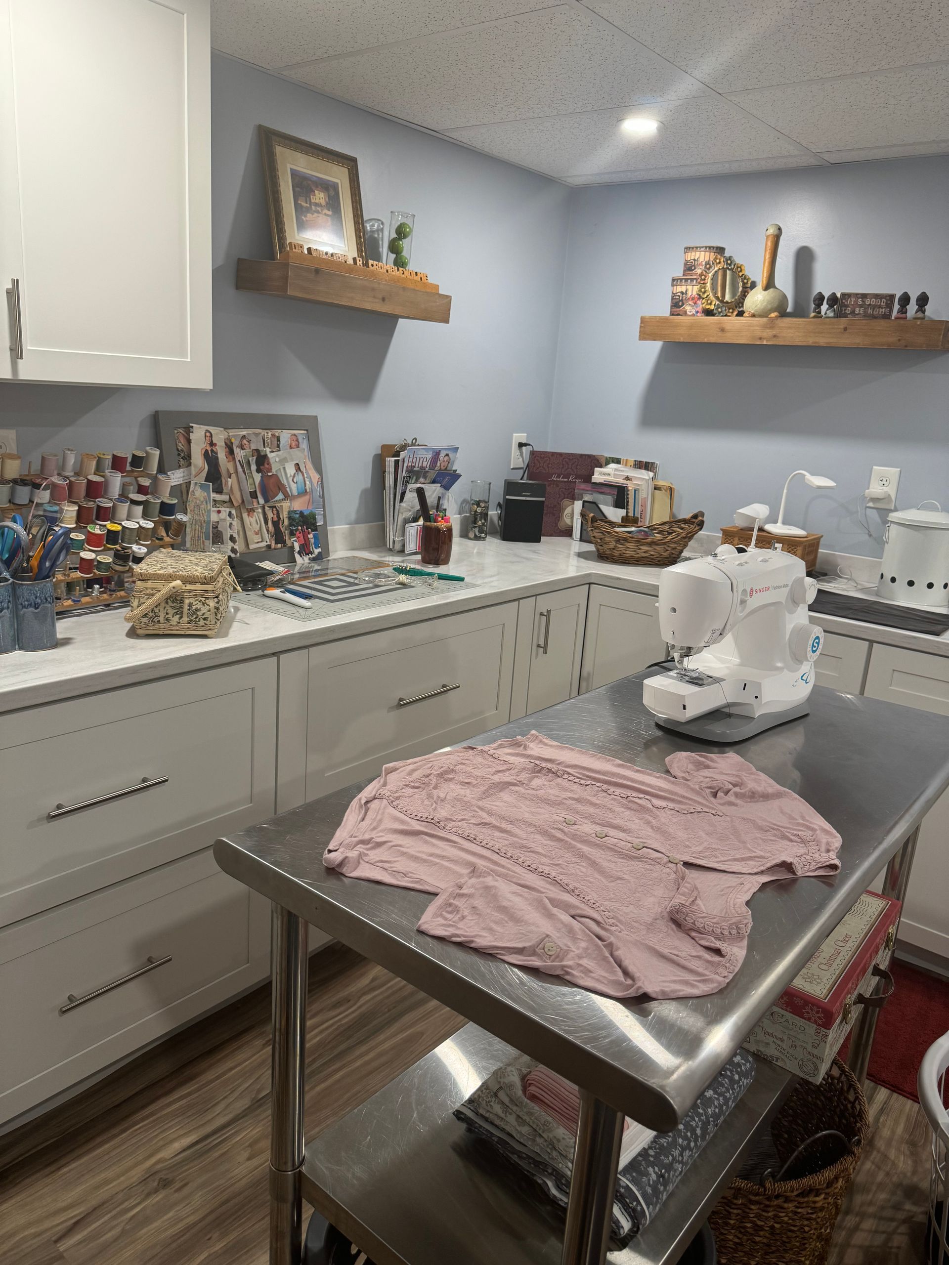 A working area for sewing with a stainless steel table, a sewing machine, and white cabinets