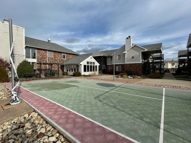 A tennis court with a basketball hoop in front of a building.