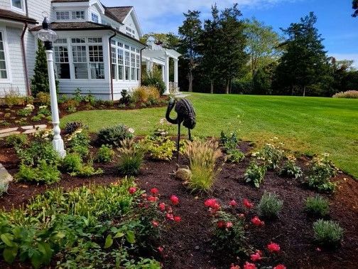 A large white house with a large lawn and flowers in front of it.