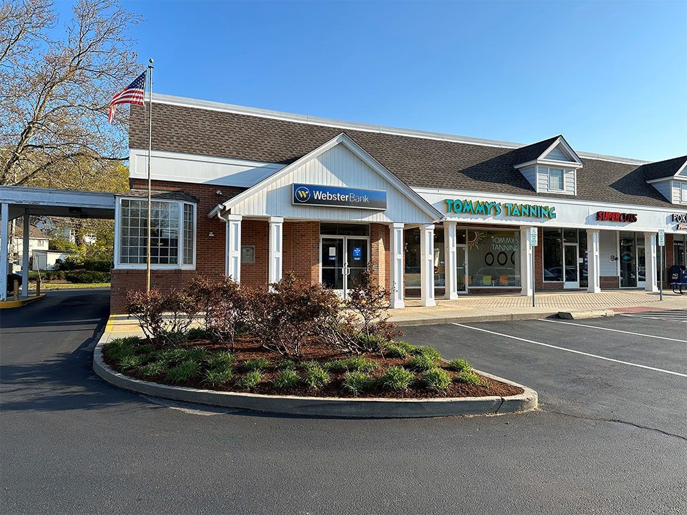 A brick building with a white roof is surrounded by other buildings and a parking lot.
