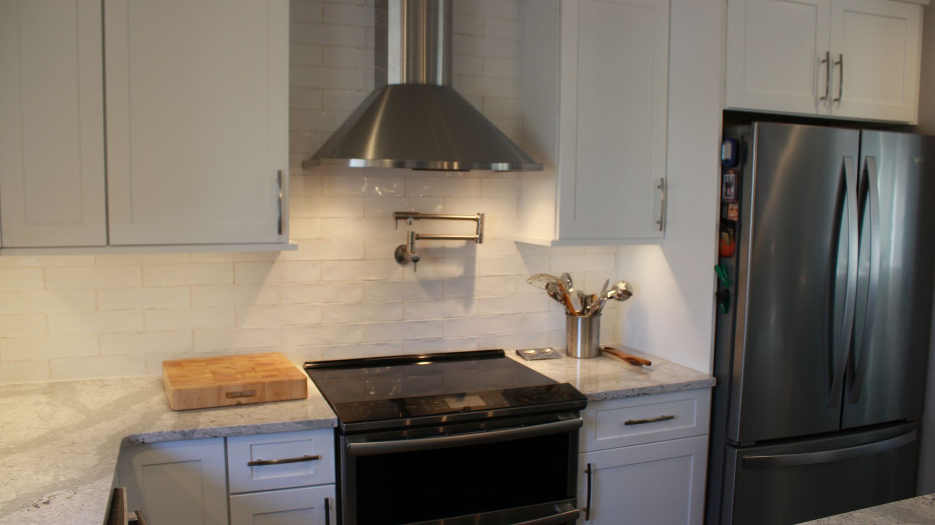 Kitchen with stainless steel hood, white cabinets, gray countertops, stove, and refrigerator.