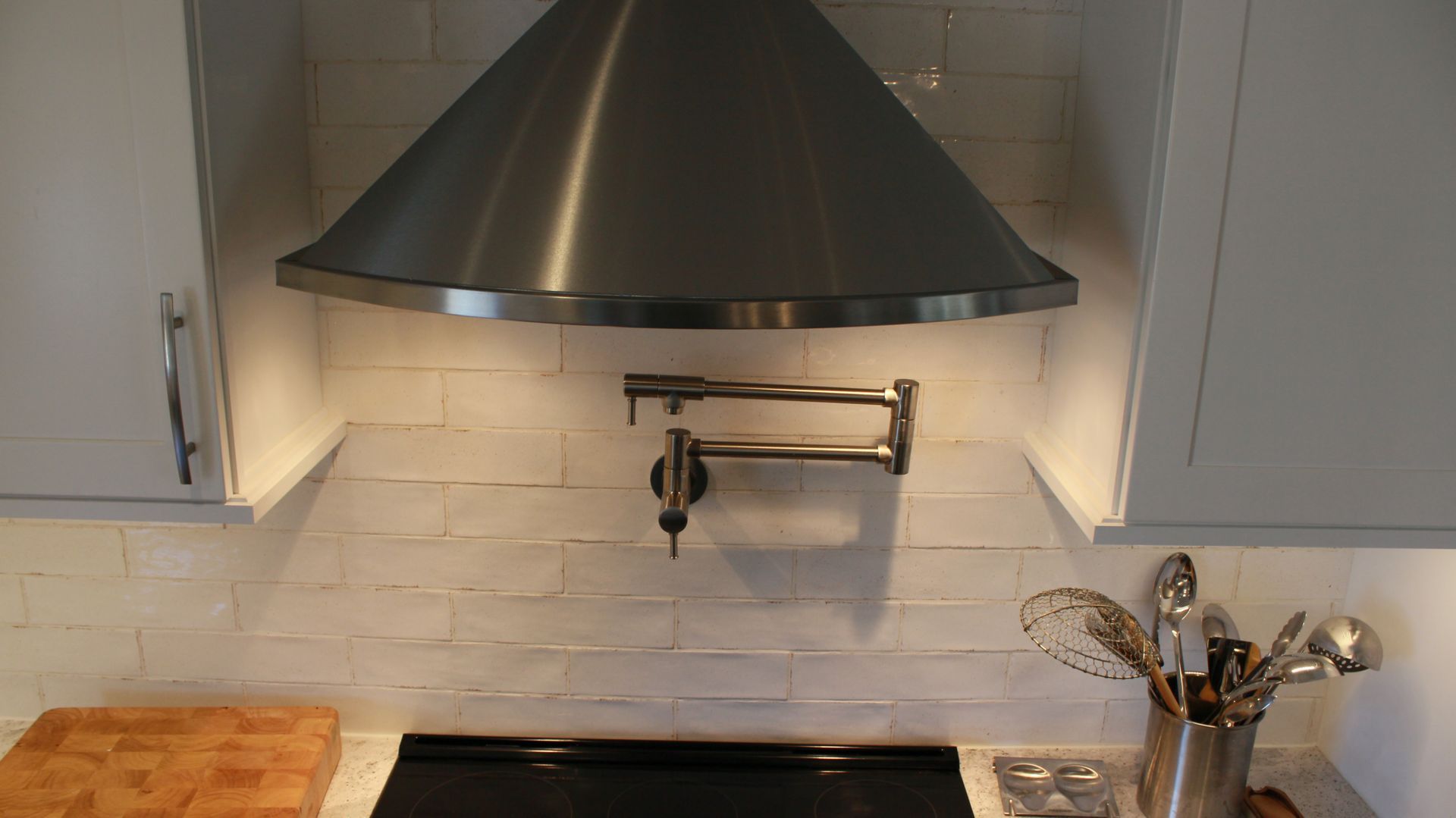 Stainless steel range hood above a cooktop on a white tile backsplash, with white cabinets on either side.