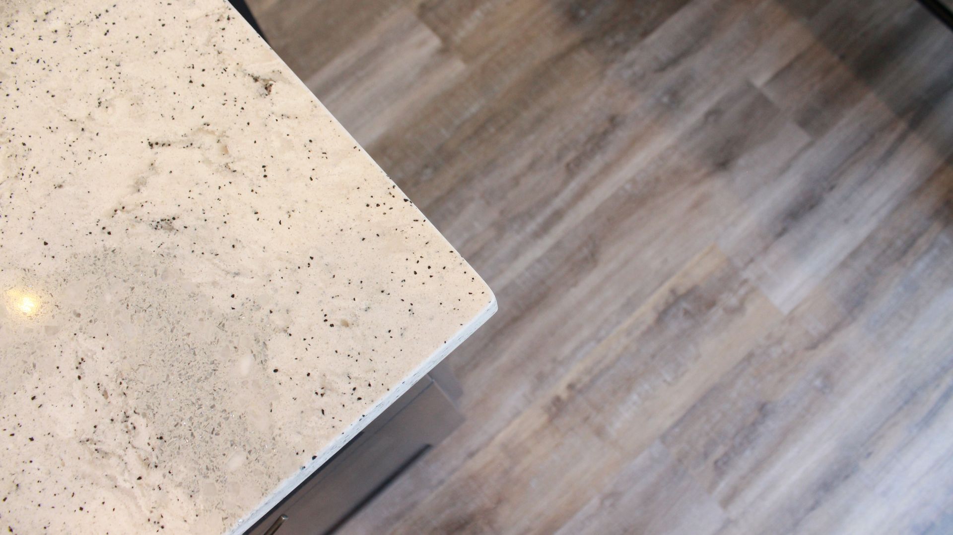 Corner of a light-colored speckled countertop with light wood-look floor.