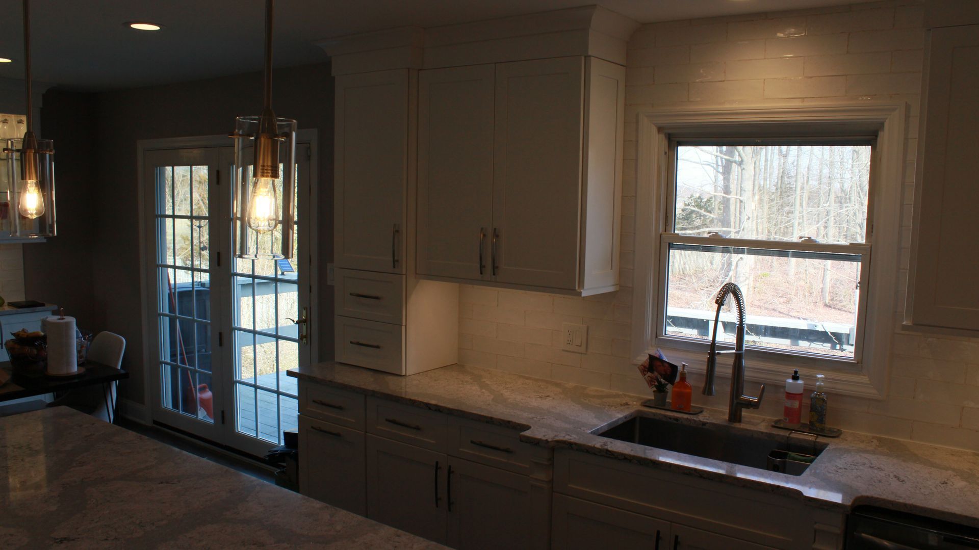 Bright kitchen with white cabinets, sink by window, and glass pendant lights.