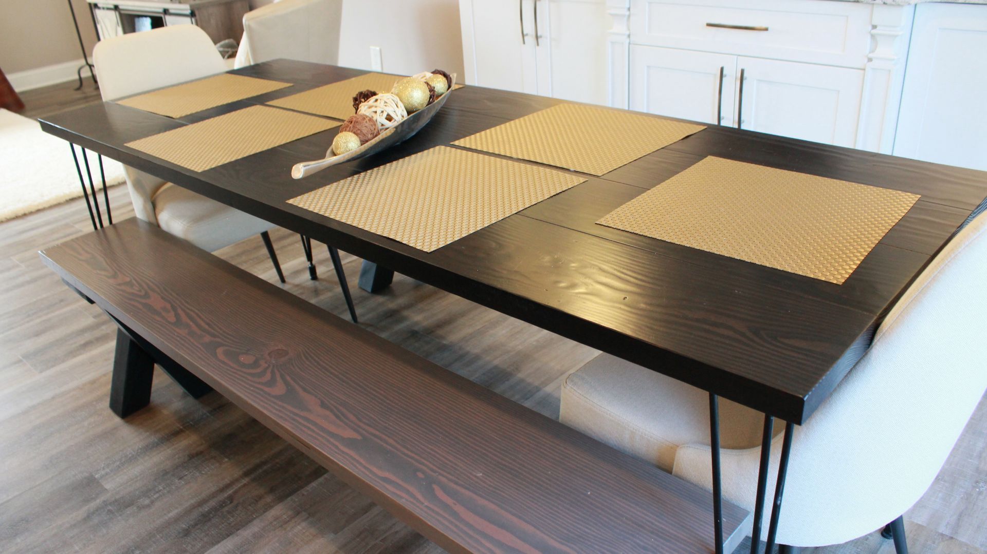 Dining table with a dark wooden top and bench, light chairs, and place mats.