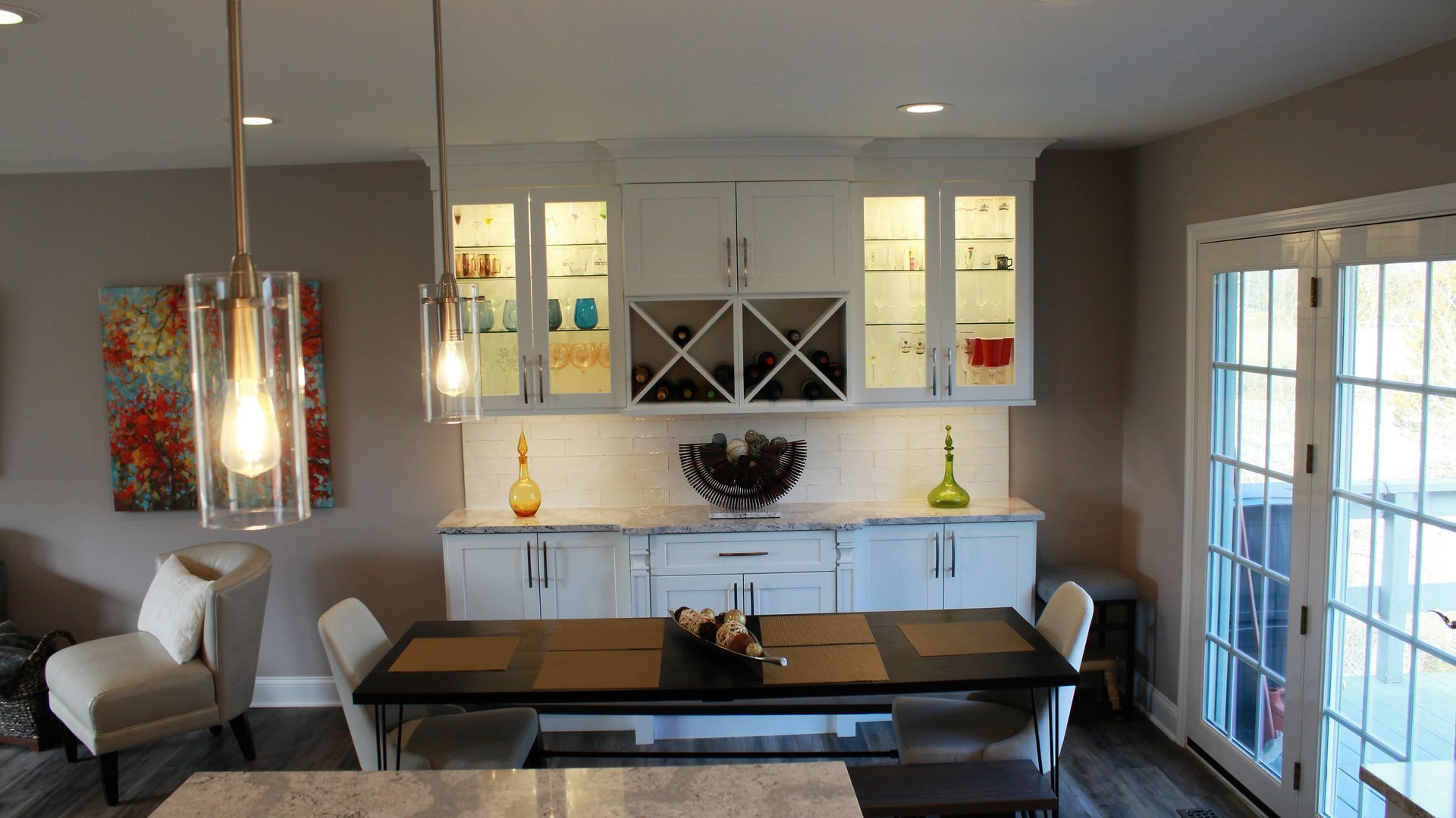 Dining room with white cabinets, wine rack, table, chairs, and glass doors.
