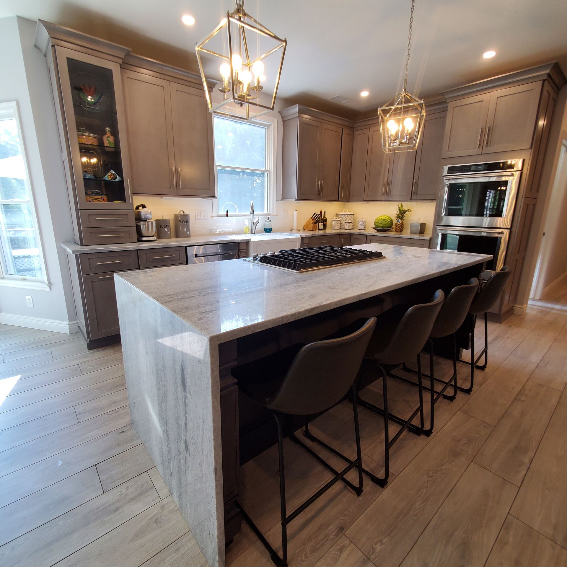 Gray kitchen with island, seating, gas cooktop, and built-in oven. Light wood floors and neutral cabinets.