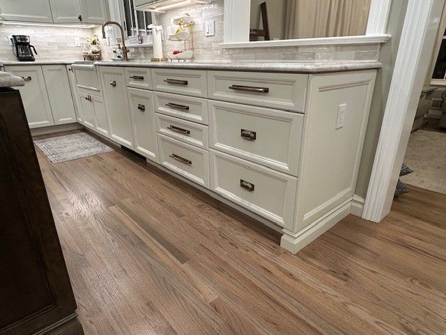 Light wood floor with white kitchen cabinets and drawers, countertop.