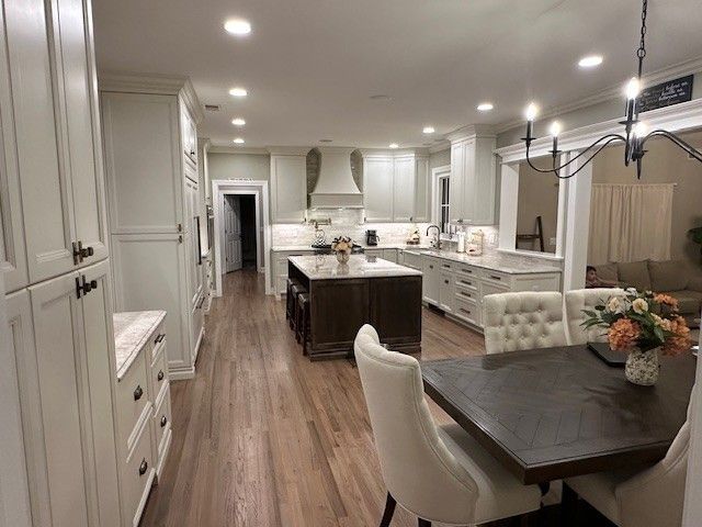 Spacious kitchen with wood floors, light cabinets, island, dining table, and built-in appliances.