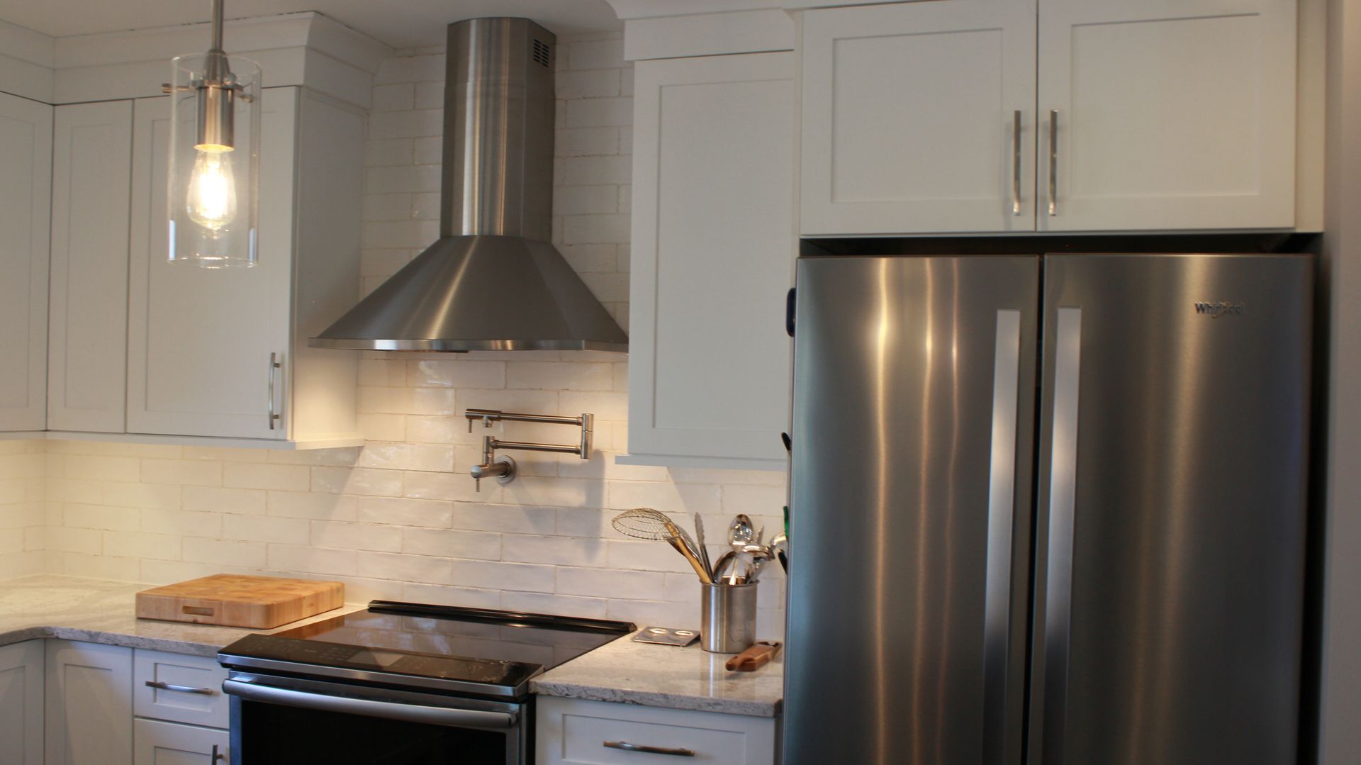 Stainless steel appliances in a white kitchen: range hood, refrigerator, cabinets, and countertop.