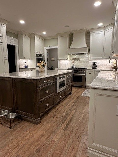 Spacious kitchen with wood floors, dark island, white cabinets, and stainless steel appliances.