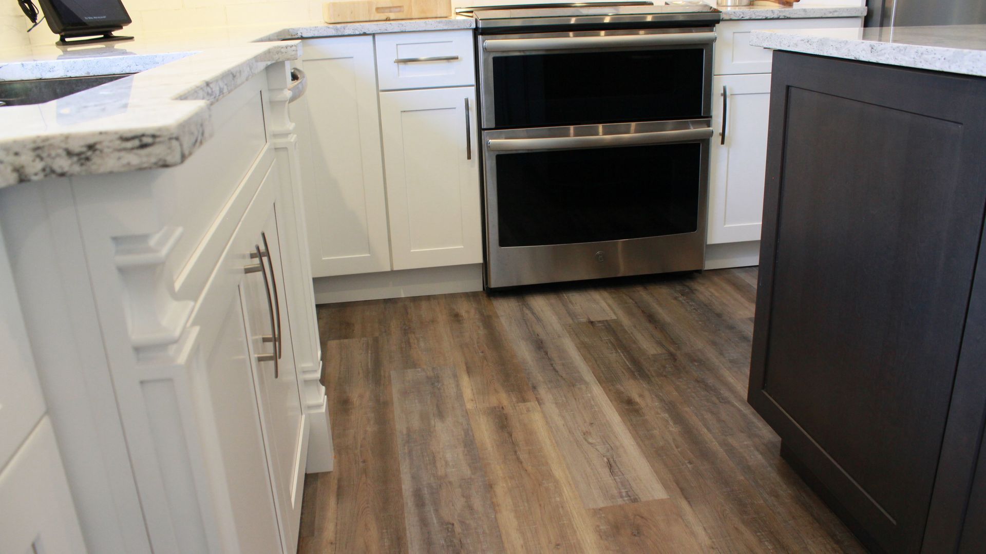 Kitchen with white cabinets, granite countertops, stainless steel oven, and wood-look flooring.