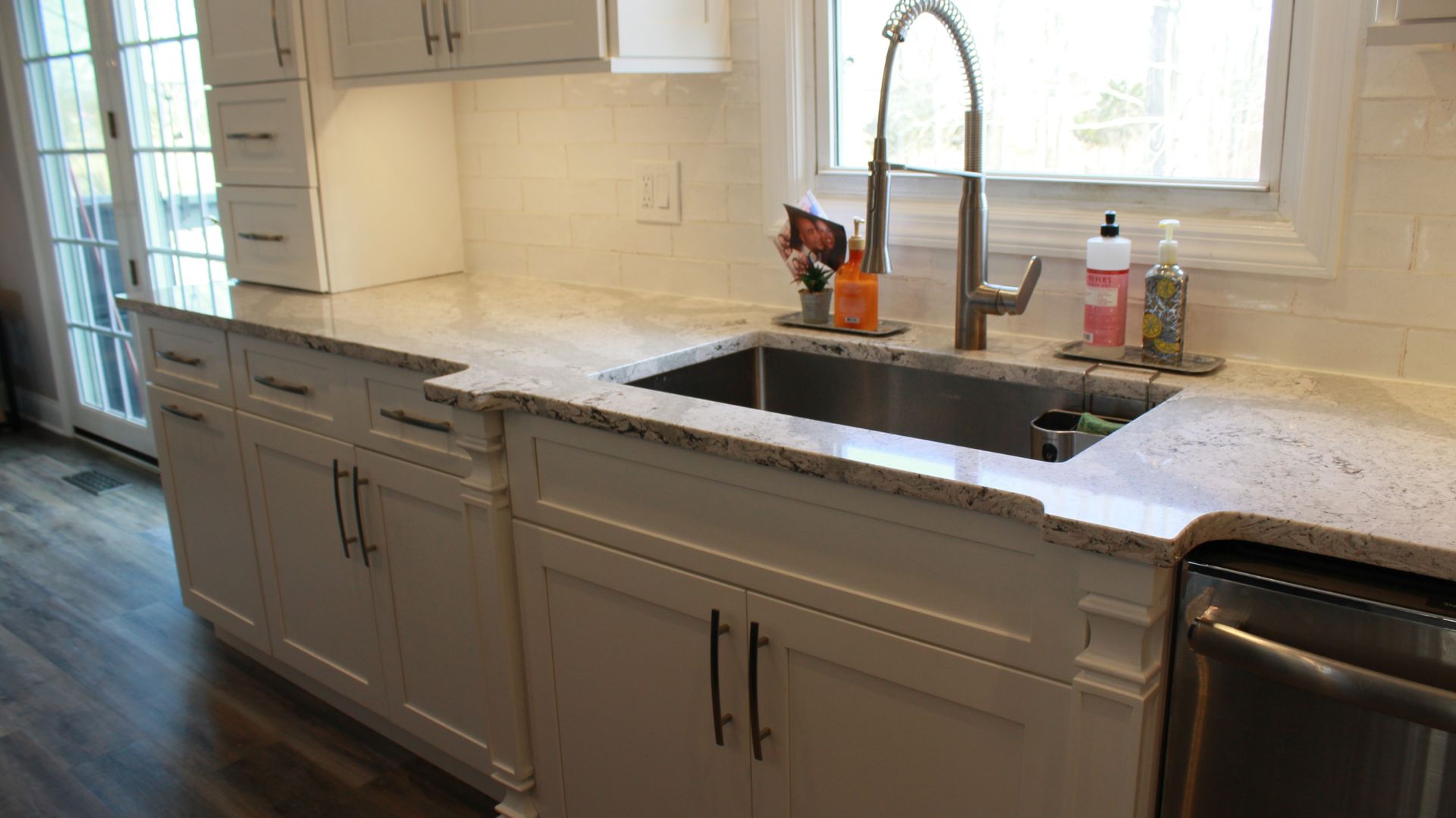 White kitchen cabinets with a stainless steel sink, faucet, and light-colored countertop.