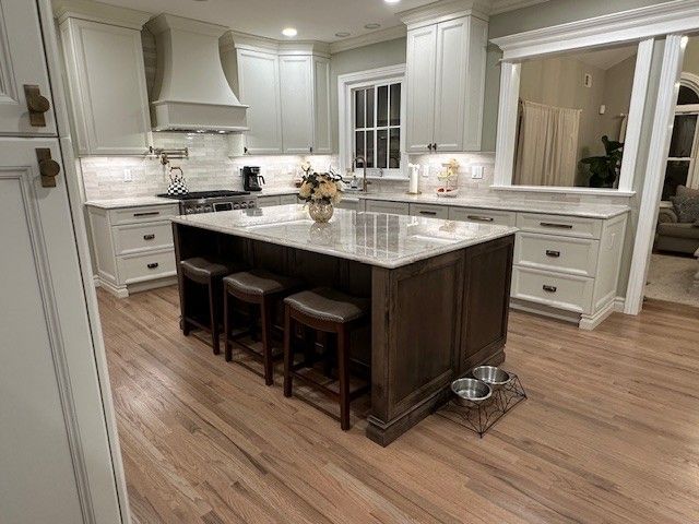 Kitchen with island, light cabinets, dark island base, and hardwood floors. Three stools sit at the island.