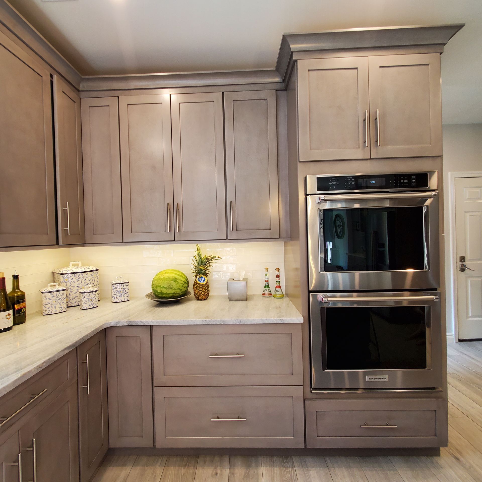 Kitchen with gray cabinets, stainless steel oven, white countertops, and light wood floor.