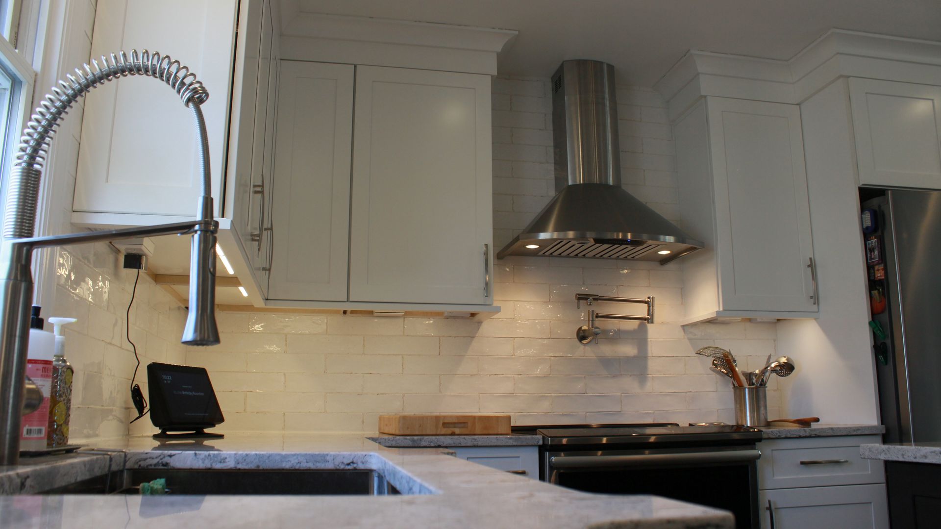 Modern kitchen with white cabinets, stainless steel range hood, and a gooseneck faucet.