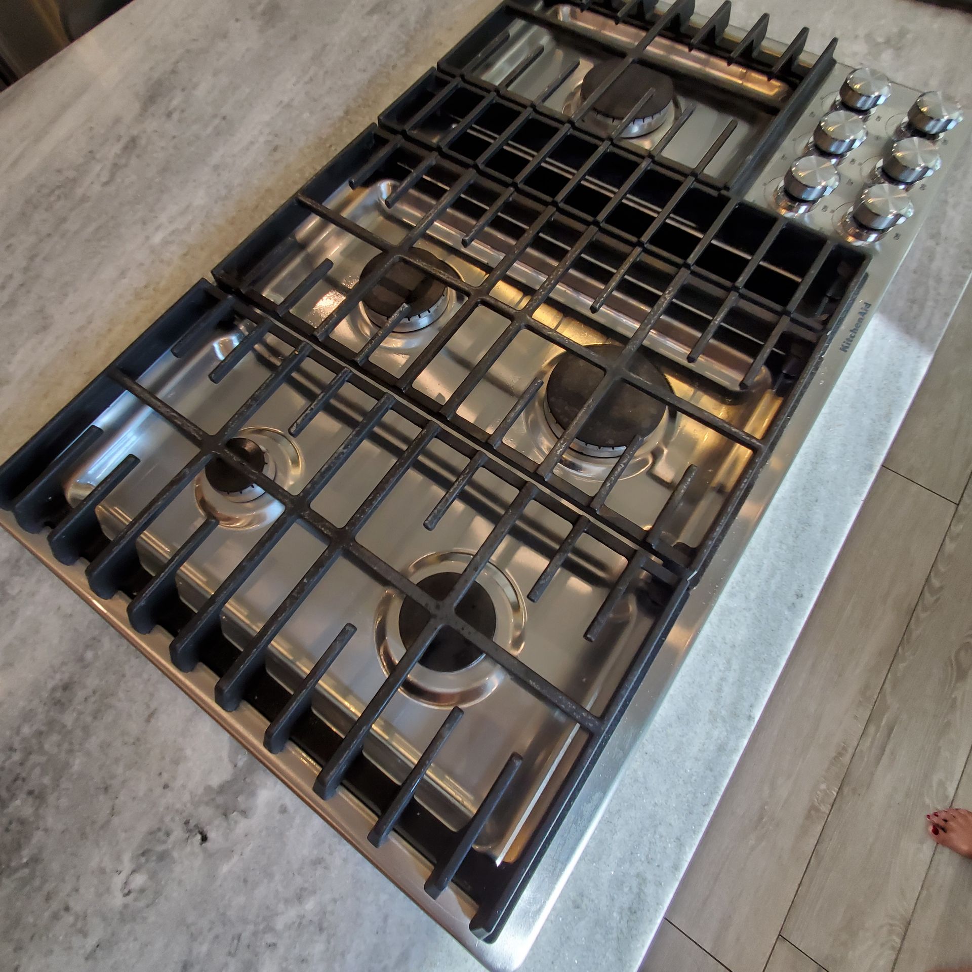 Stainless steel gas cooktop with black grates and knobs on a gray countertop.
