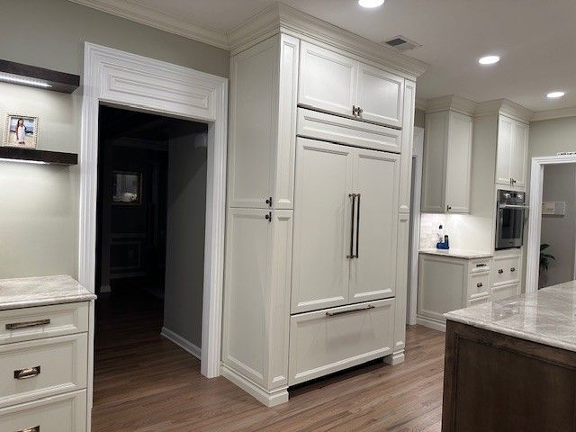 White kitchen with refrigerator and cabinets; a doorway on the left.