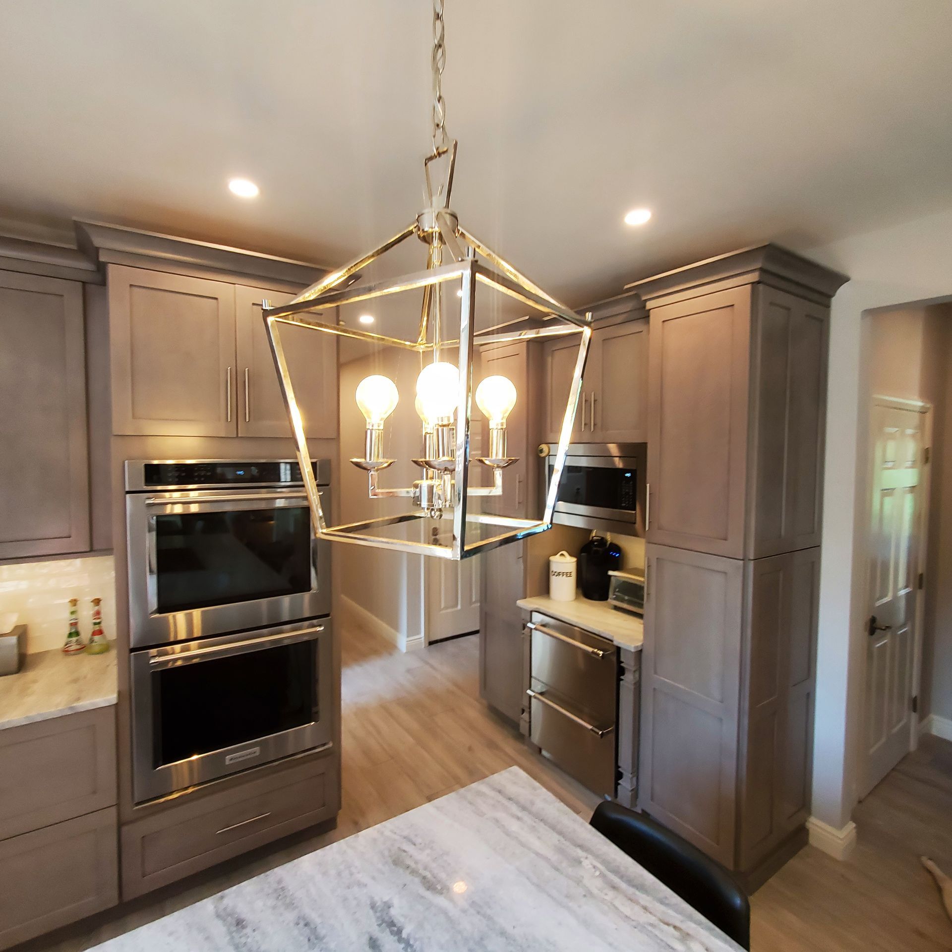 Modern kitchen with grey cabinets, stainless steel appliances, and geometric chandelier.