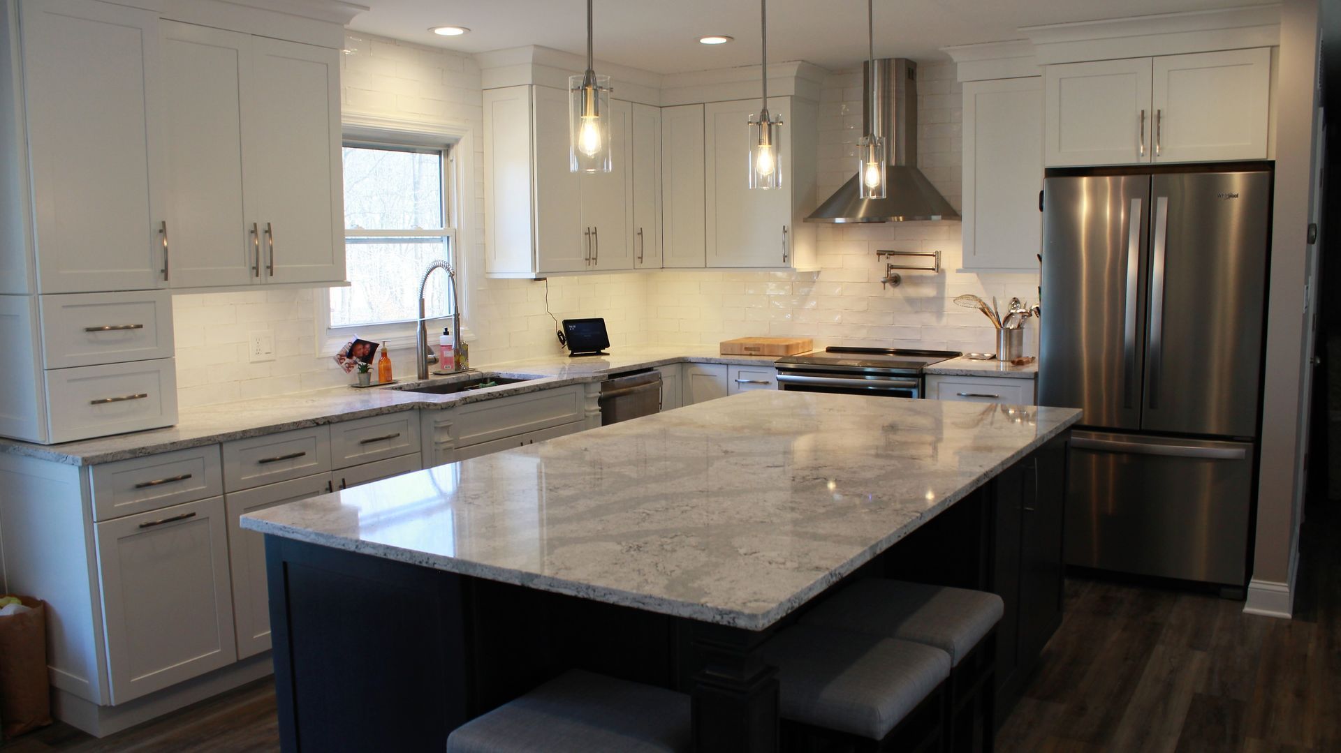 Modern white kitchen with a granite island and stainless steel appliances.