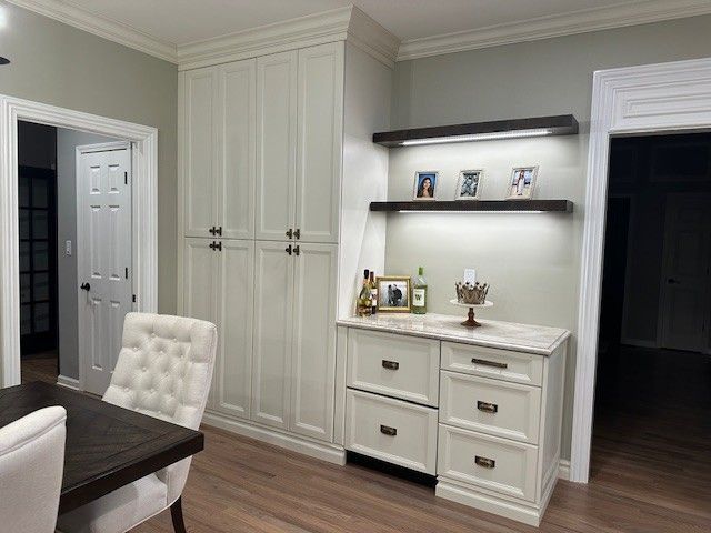 Built-in cabinets, desk with drawers, shelves with lights, and a dining room with a table and chair.
