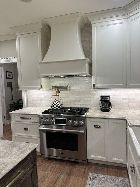 White kitchen with a stainless steel stove, range hood, and cabinets.