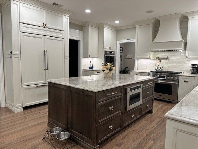 Spacious kitchen with a dark brown island, white cabinets, stainless steel appliances, and wood floors.