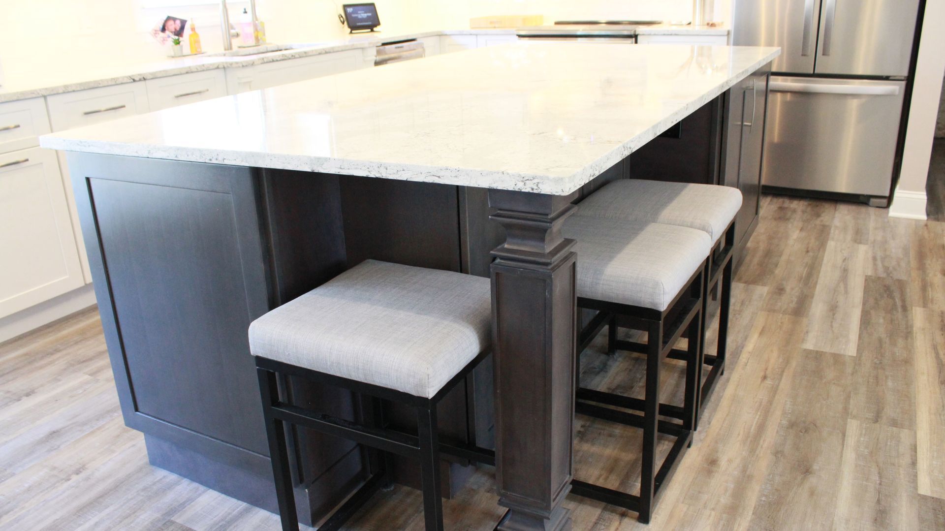 Kitchen island with dark gray cabinets, white countertop, and two gray-cushioned bar stools.