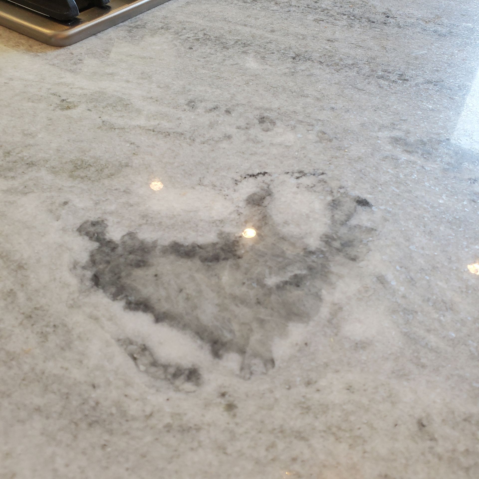 Close-up of a white marble countertop with a large, dark gray stain in the center. Shiny surface.