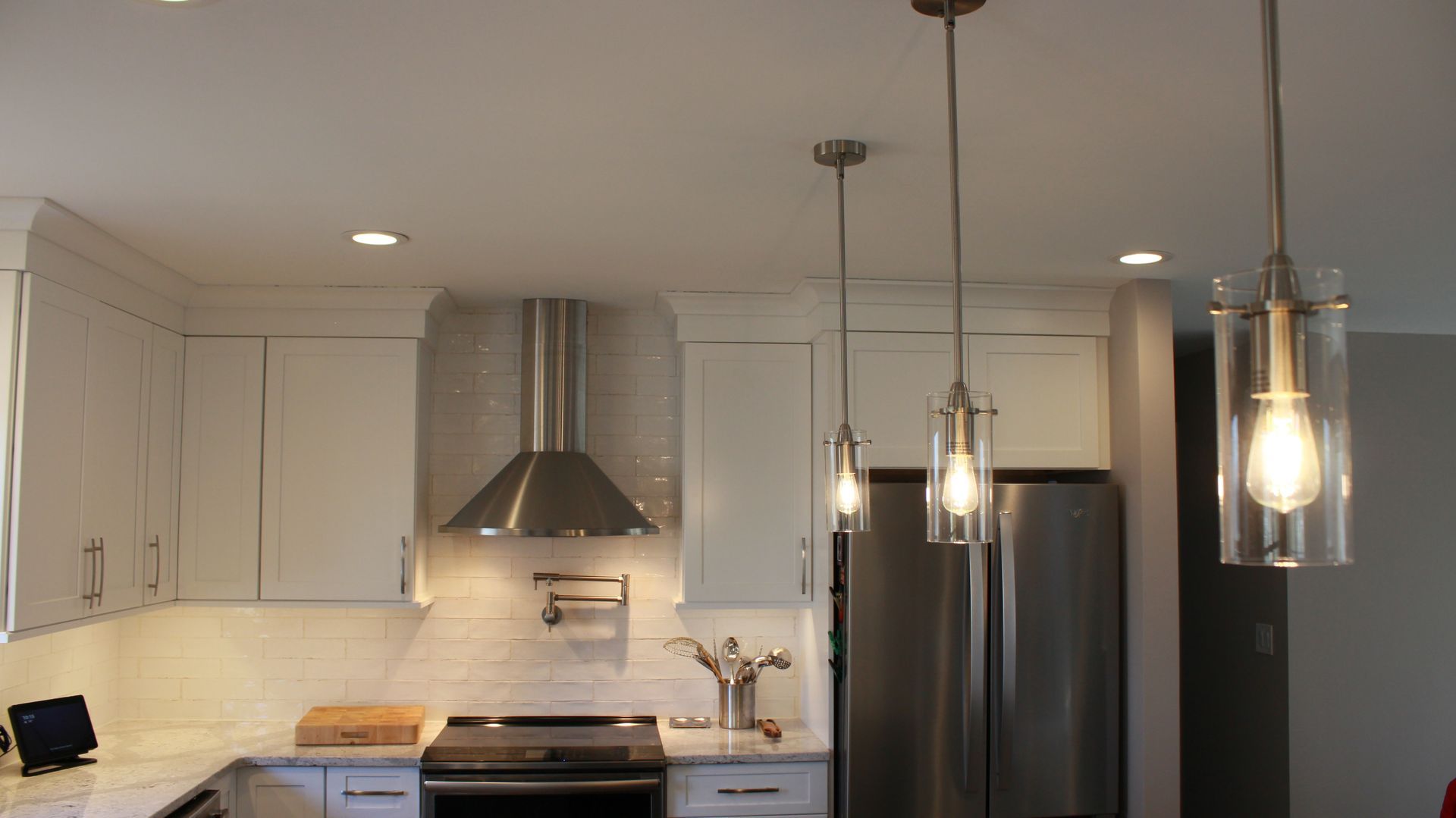 Kitchen with white cabinets, stainless steel appliances, pendant lights, and a range hood.