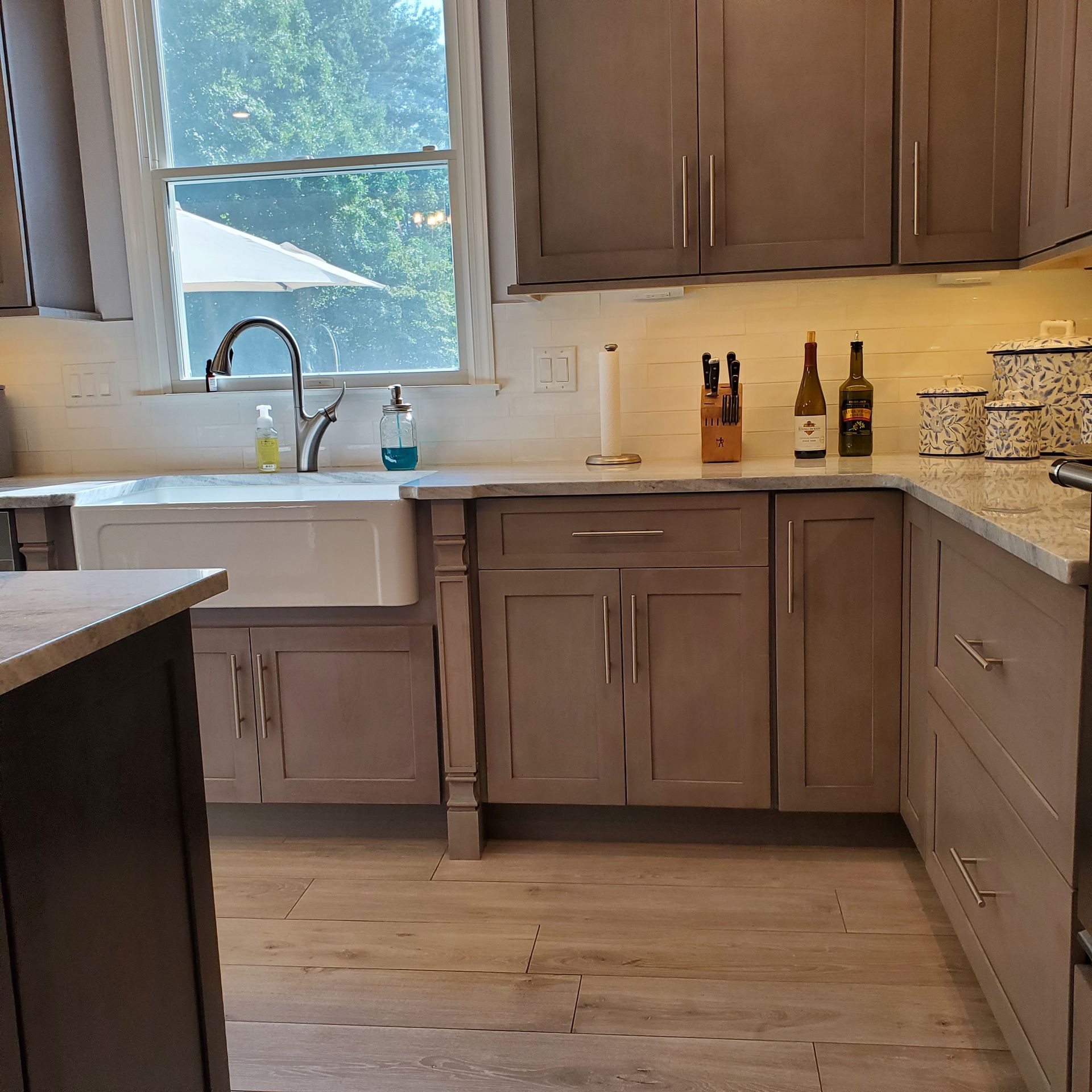 Kitchen with gray cabinets, farmhouse sink, window, granite countertops, and wood-look floor.