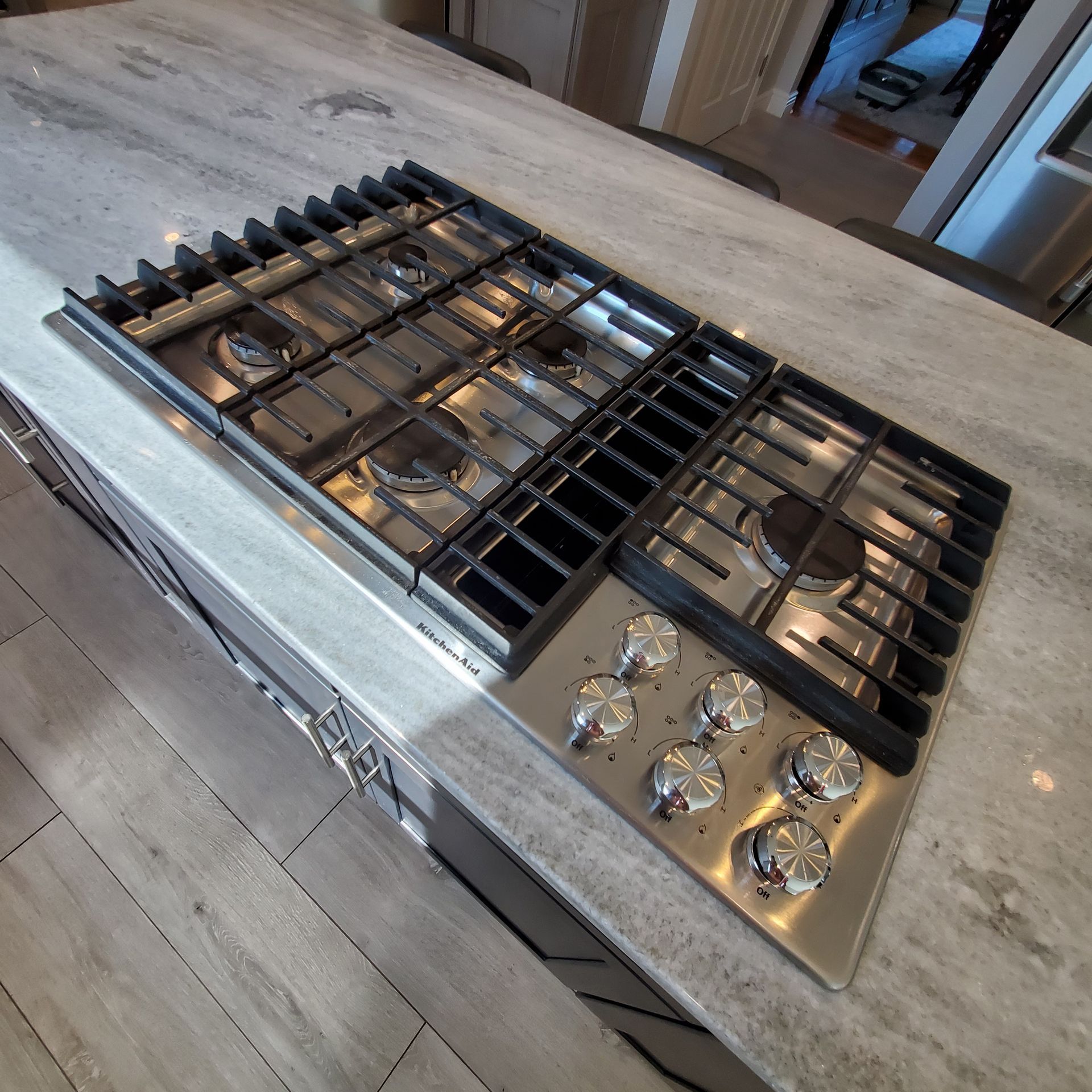 Gas cooktop built into a grey countertop with stainless steel knobs and black grates.