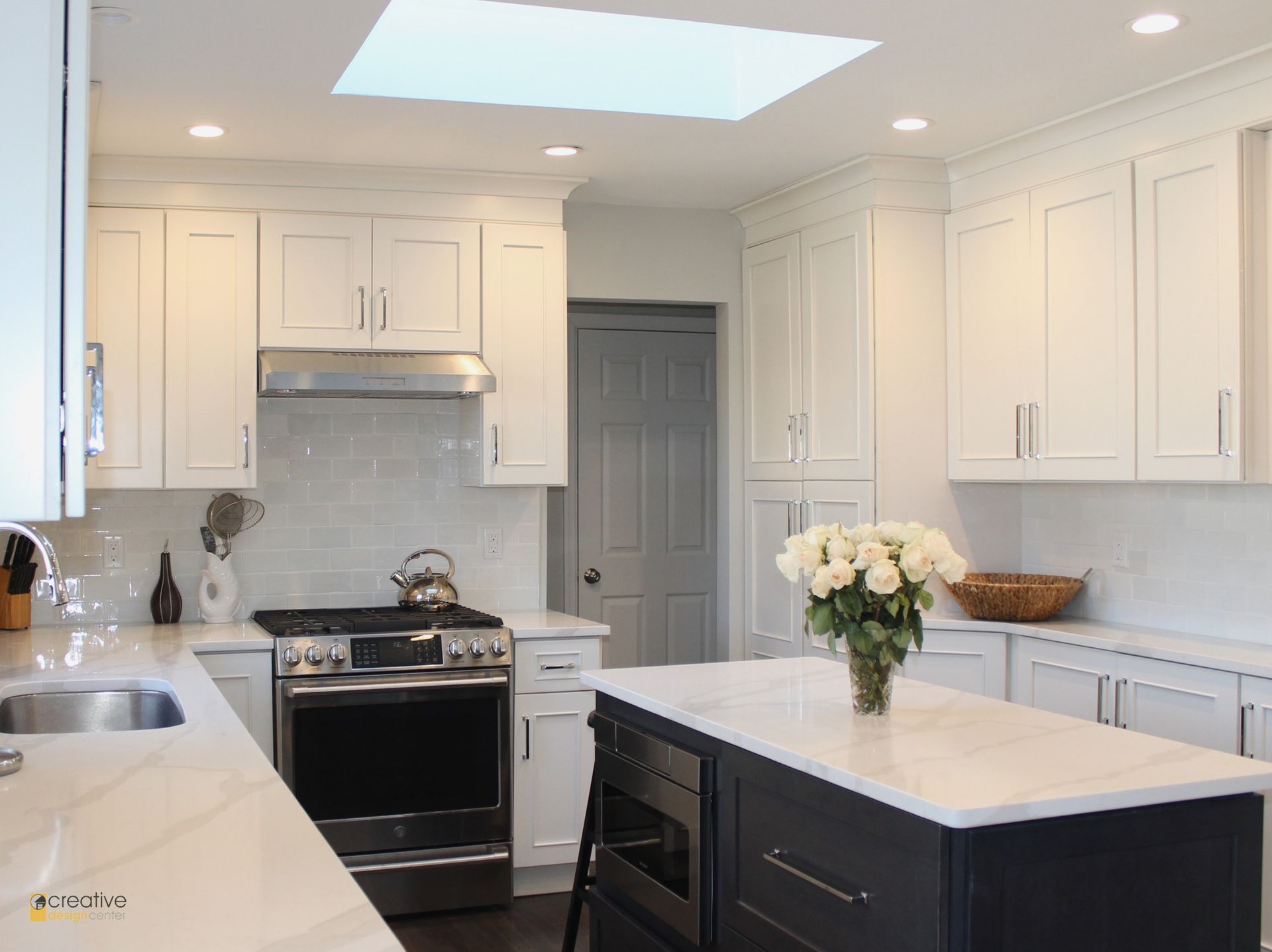 A kitchen with white cabinets, a black island, a stove, a sink, and a skylight.