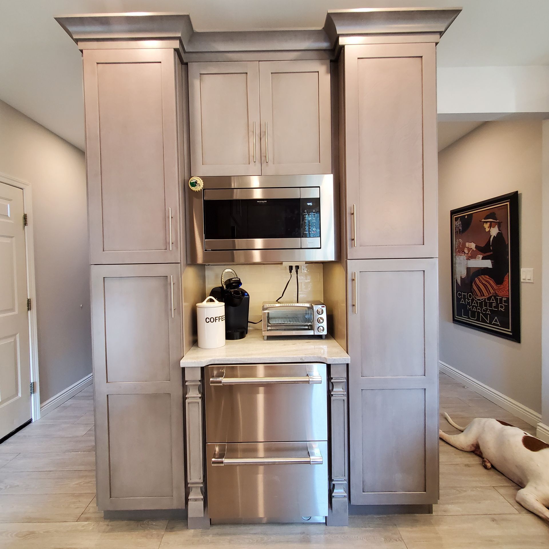Gray kitchen cabinets with microwave, under-counter fridge, and small appliances. Dog relaxes on the floor.