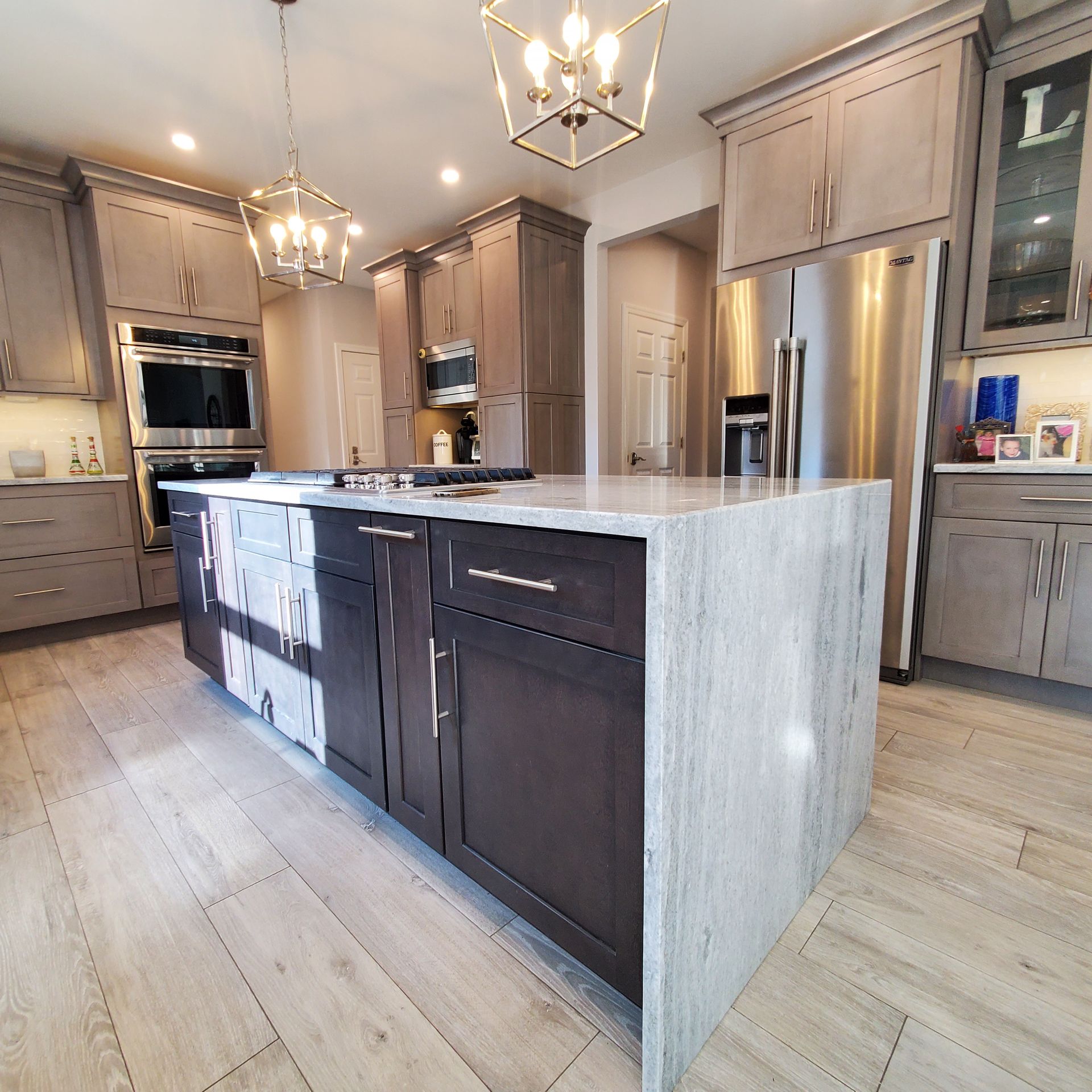 Modern kitchen with gray and dark cabinets, island, stainless steel appliances, and light wood-look flooring.