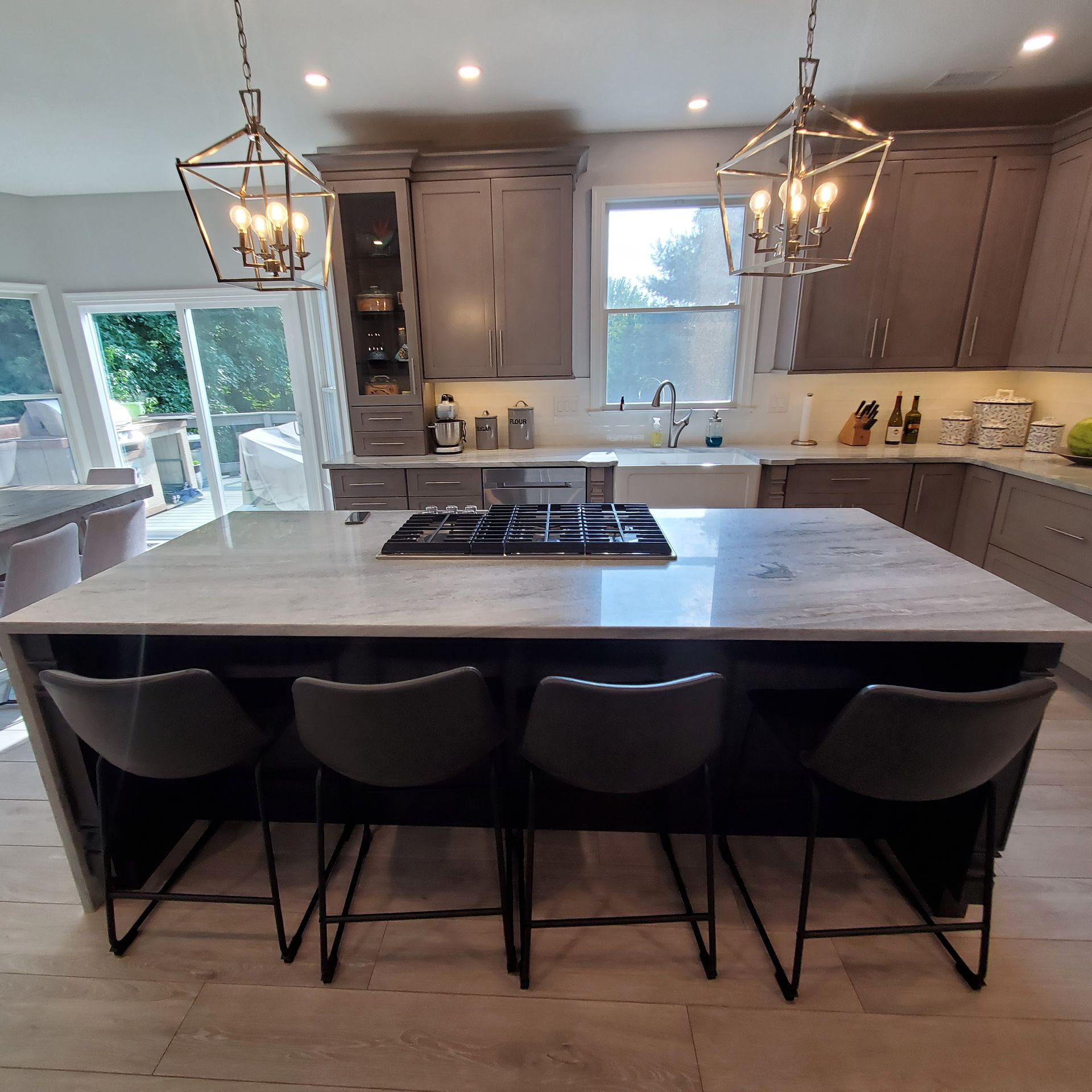 Modern kitchen with gray cabinets, island with cooktop, four bar stools, and pendant lights.