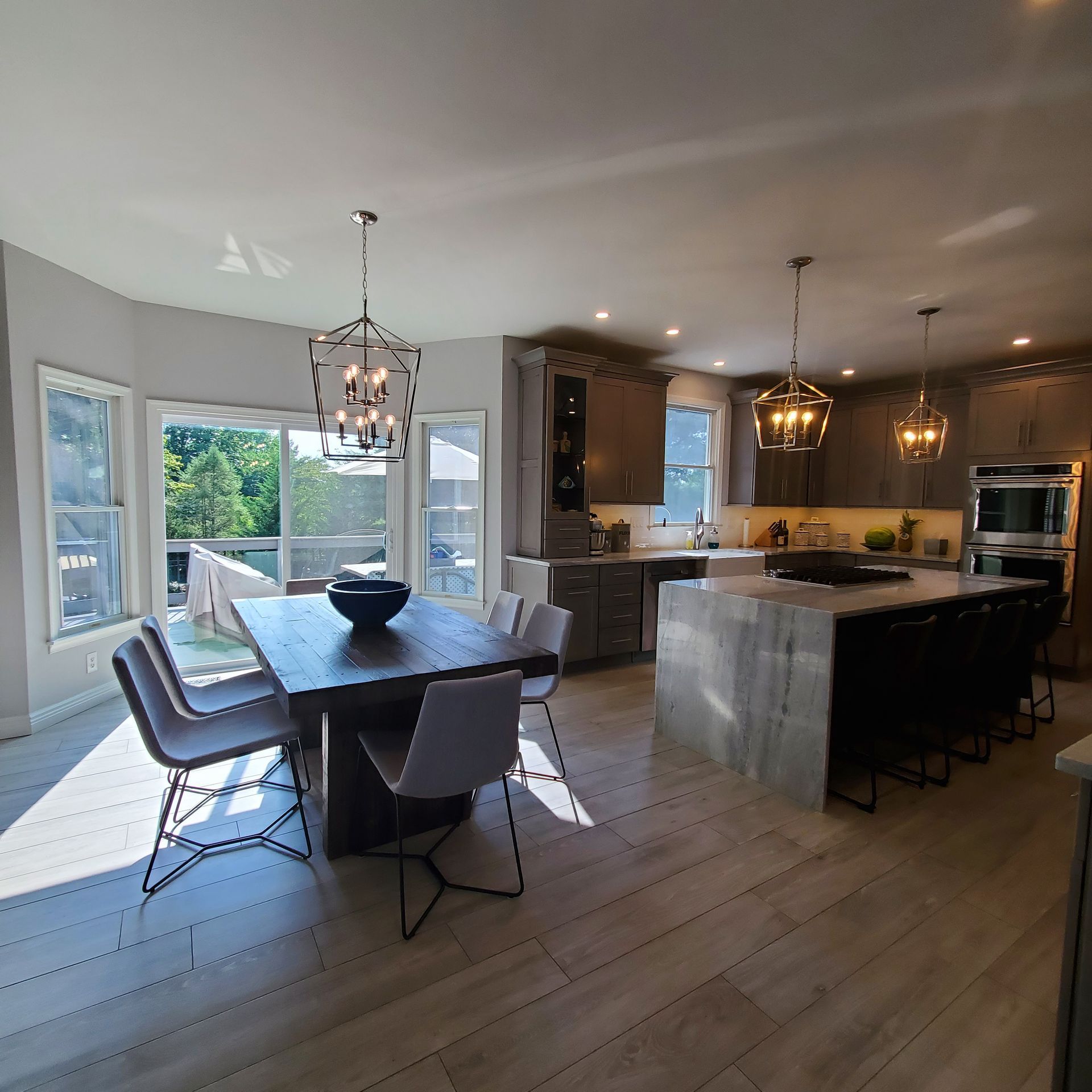 Modern kitchen with dining area. Gray cabinets and island, wooden table, and light fixtures.