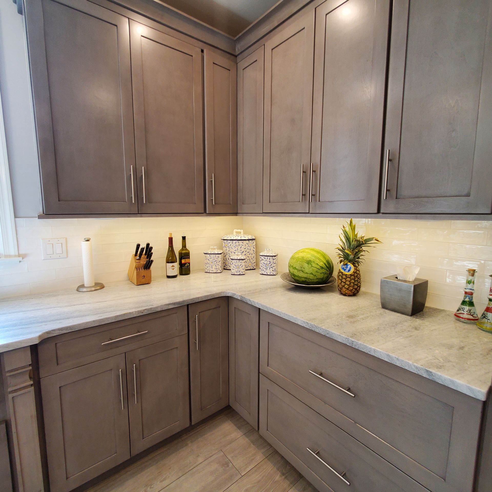 Gray kitchen cabinets with light countertops, under-cabinet lighting, and various kitchen items.