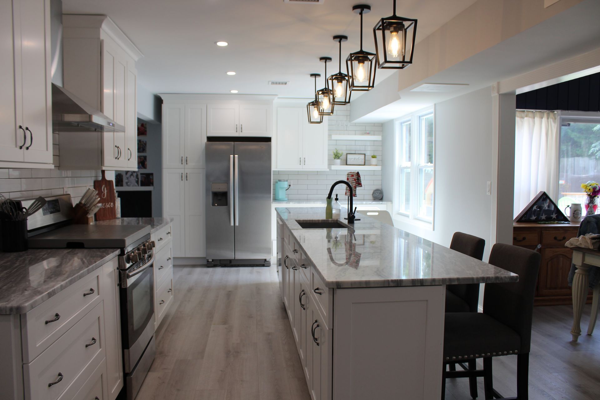 Modern white kitchen with a marble countertop island and black pendant lights.