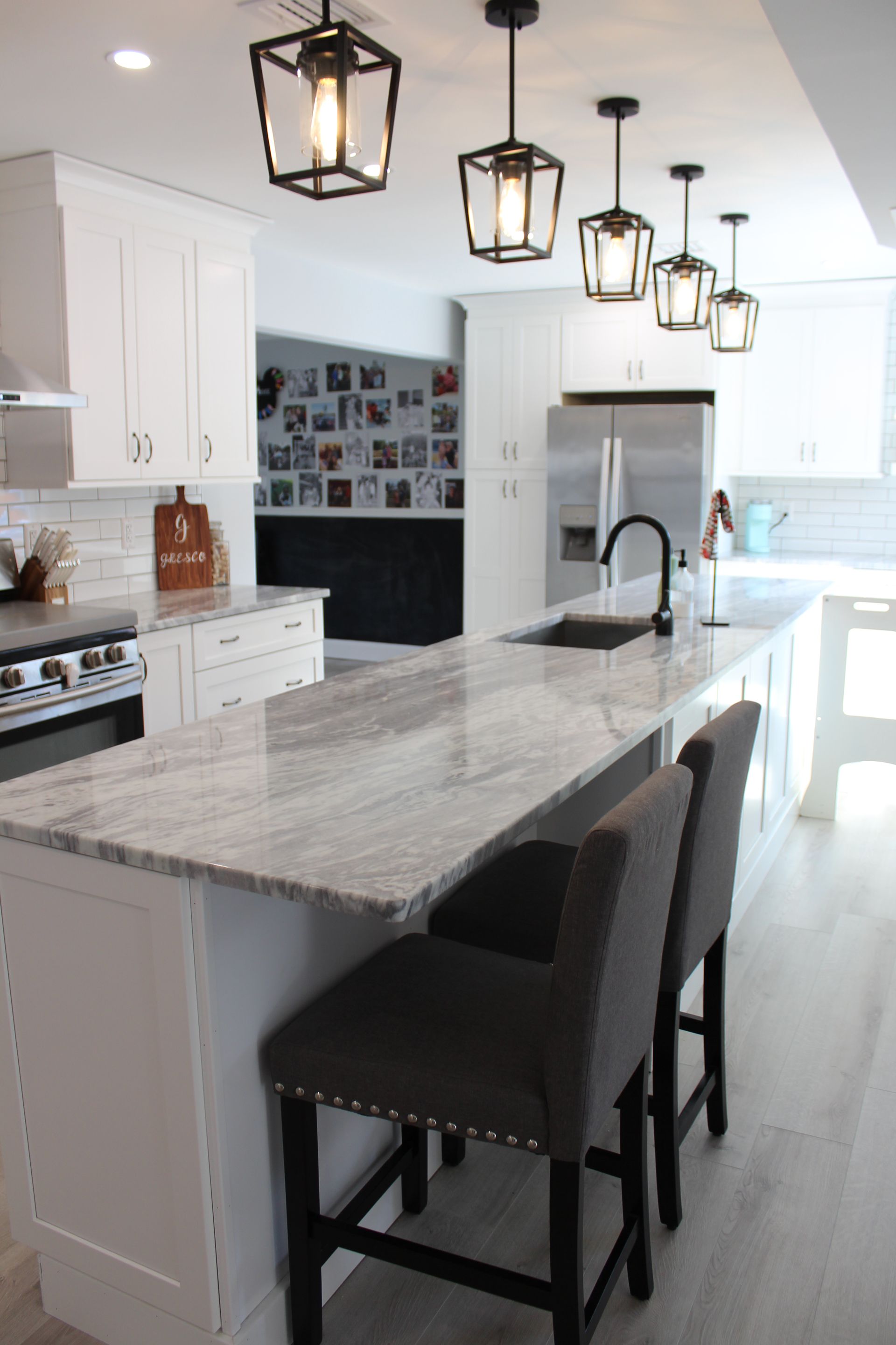 Modern white kitchen with marble island, black pendant lights, and gray bar stools.