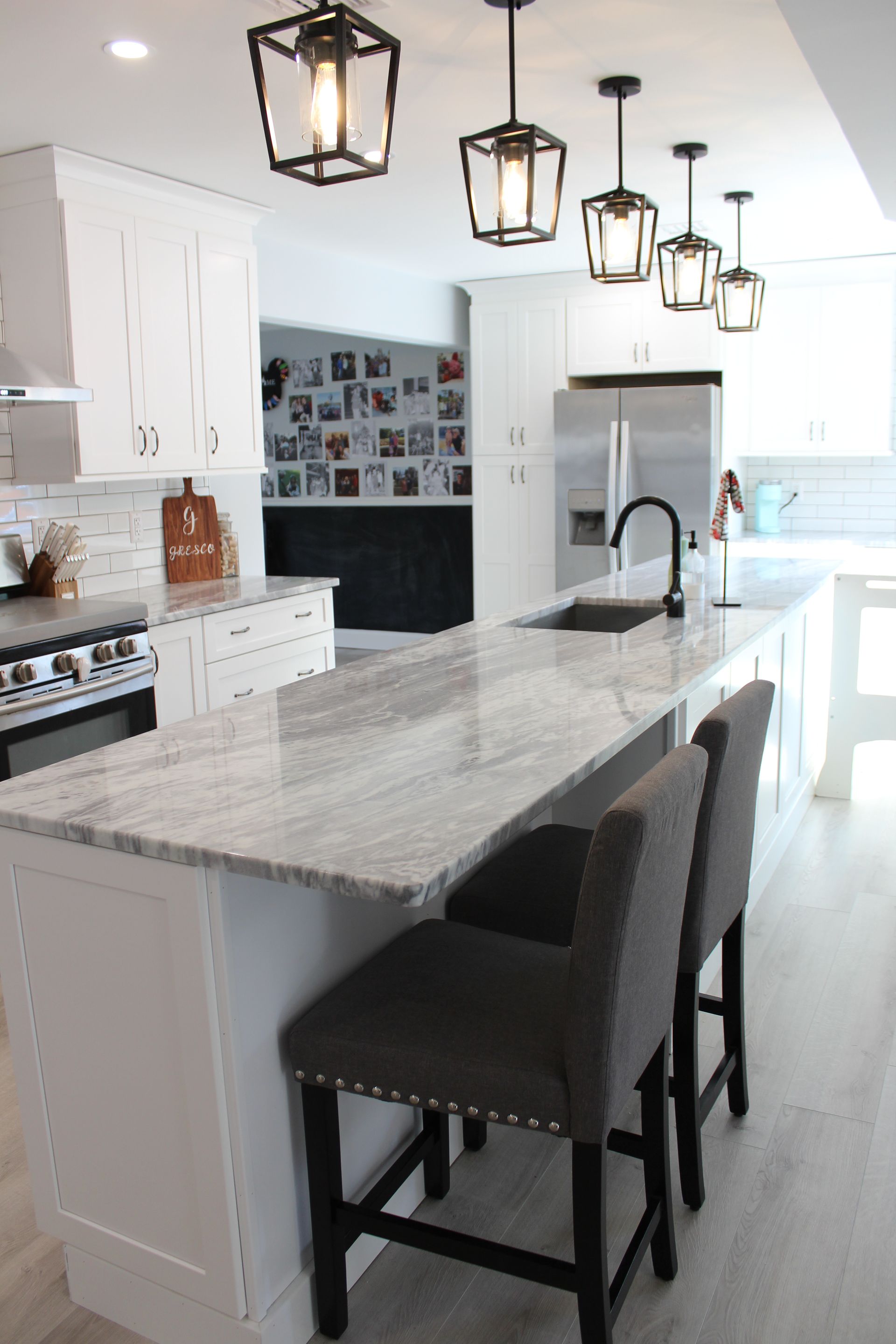 Modern white kitchen with a granite island, black pendant lights, and two gray bar stools.