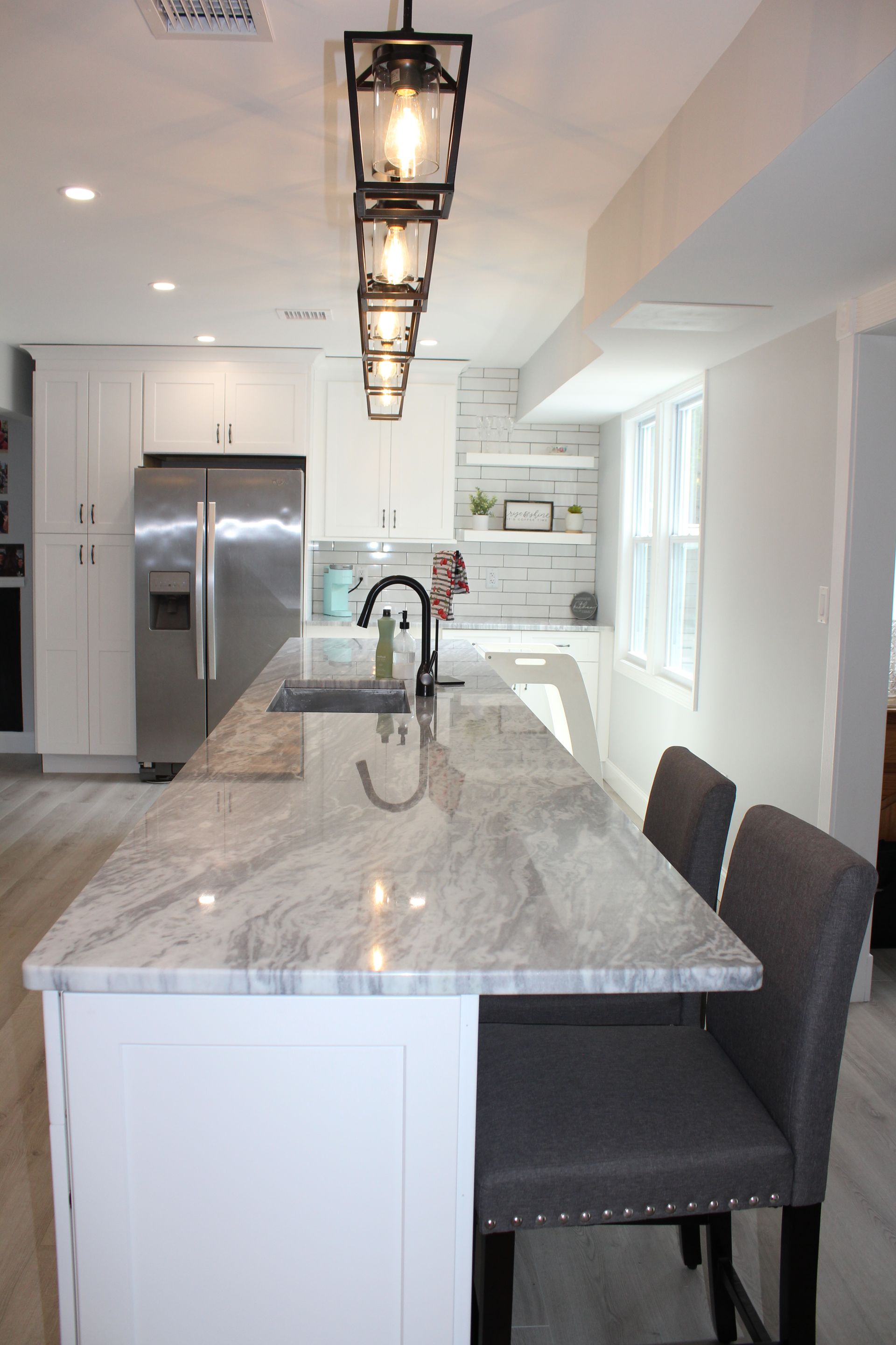 Bright white kitchen with island, stainless steel fridge, and pendant lights.