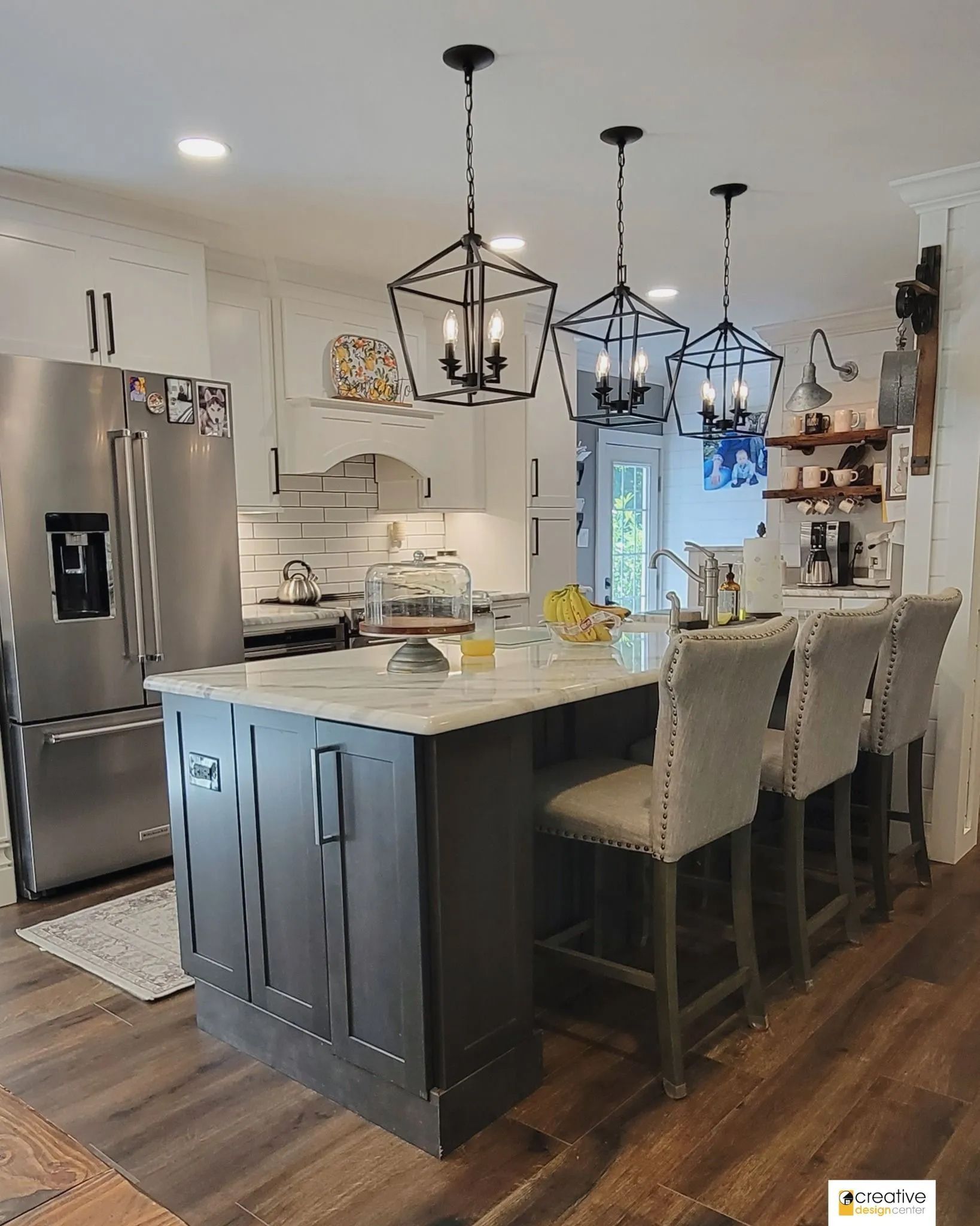 A kitchen with a large island, stools and a refrigerator.
